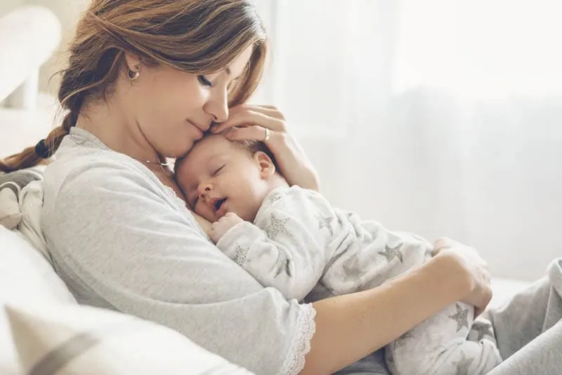 Junge hübsche Mutter hält schlafendes Baby an der Brust