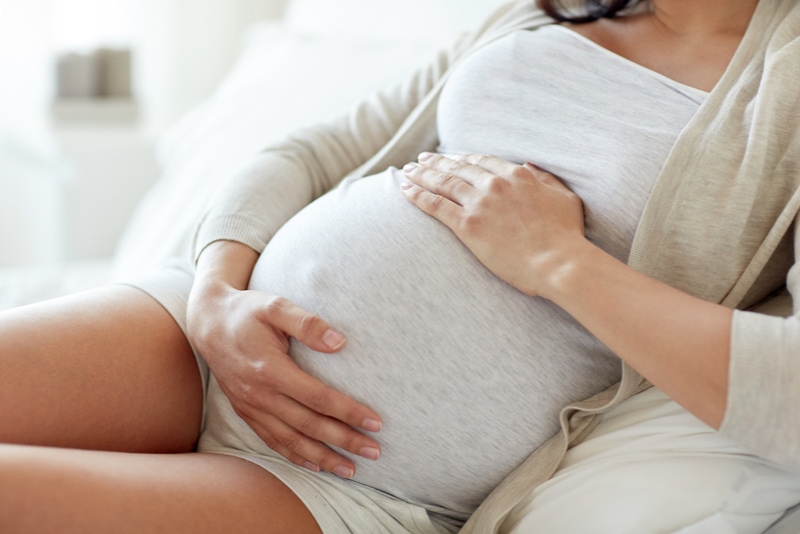 schwangere Frau, die auf Bett sitzt und ihren Bauch zu Hause berührt