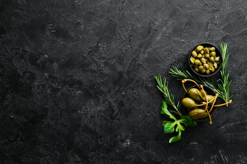 Marinated capers in a bowl on a black stone background