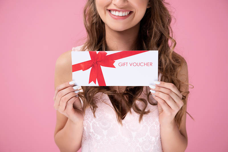 Lächelnde junge Frau hält einen Geschenkgutschein in den Händen