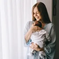 glückliche junge Mutter hält neugeborenes Baby am Fenster