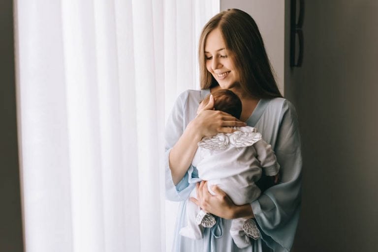 glückliche junge Mutter hält neugeborenes Baby am Fenster
