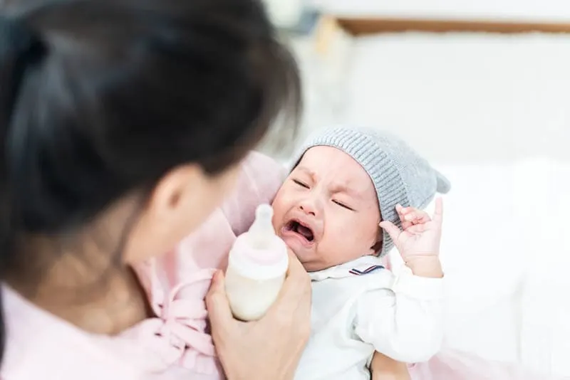 Mutter hält Milchflasche und weinendes Baby mit Hut