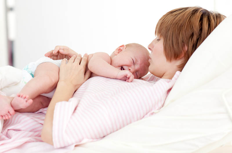Mutter liegt auf dem Bett und hält auf ihrer Brust weinende Baby in Windeln