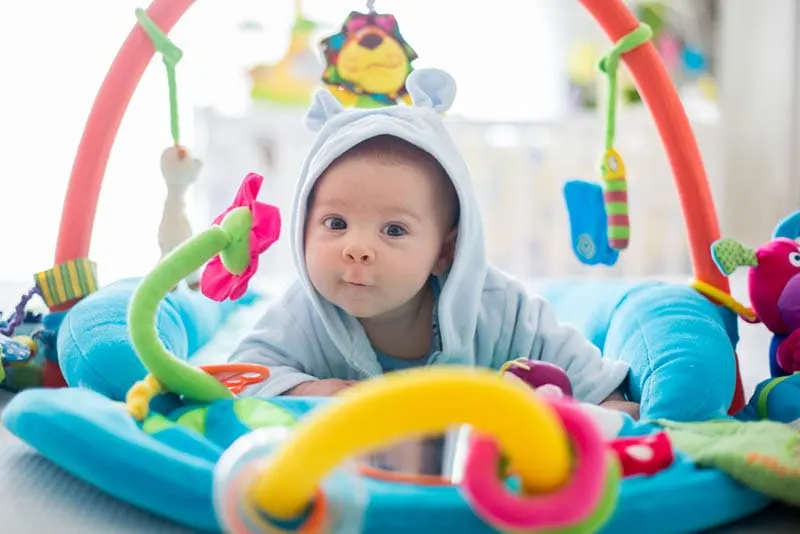 Nettes Baby Junge auf dem Bauch spielen mit hängenden Spielzeug 
