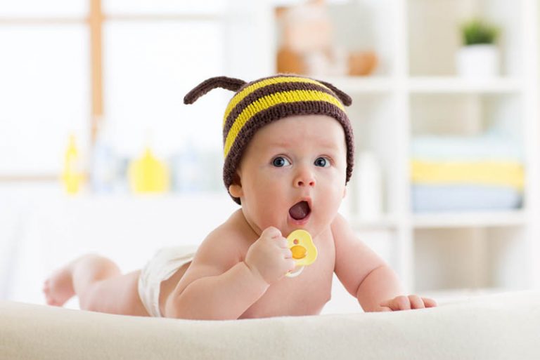 Baby liegt auf dem Bett und hält einen Schnuller in der Hand