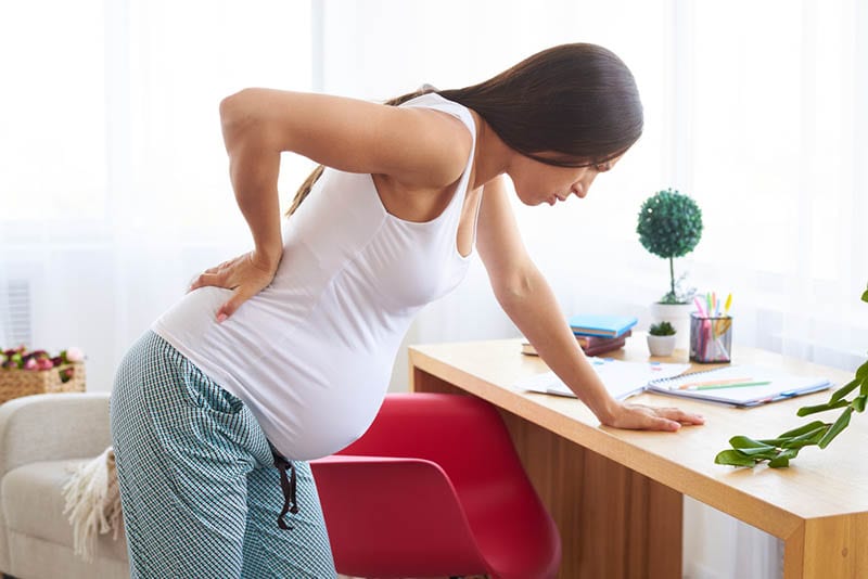 Schwangere Frau fühlt Rückenschmerzen und hält für Tisch zu Hause