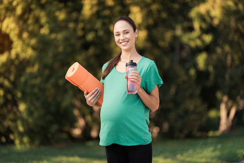 Schwangere Frau zu Fuß im Park mit einer Sportflasche in den Händen