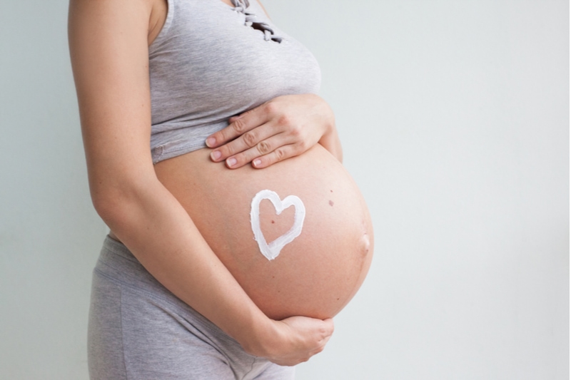 Schwangere trägt Dehnungsstreifencreme auf ihren Bauch auf