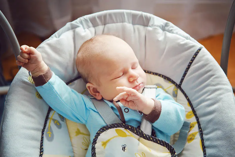 Süßer Babyjunge schläft in einer Babywippe mit Gurten