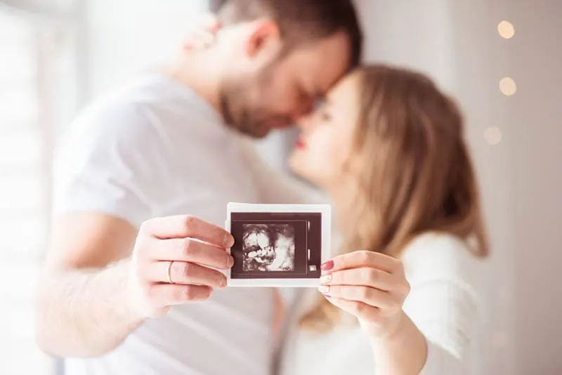 Verliebtes Paar, das sich umarmt und ein Ultraschallbild ihres Babys hält