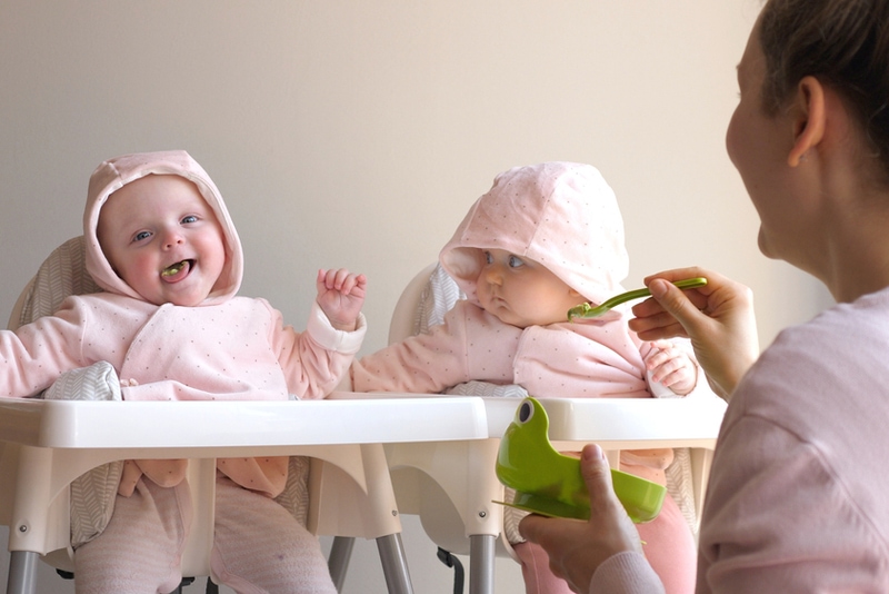Mutter füttert lustige fröhliche Baby-Zwillinge