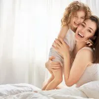 glückliche Mutter und Tochter umarmen sich auf dem Bett