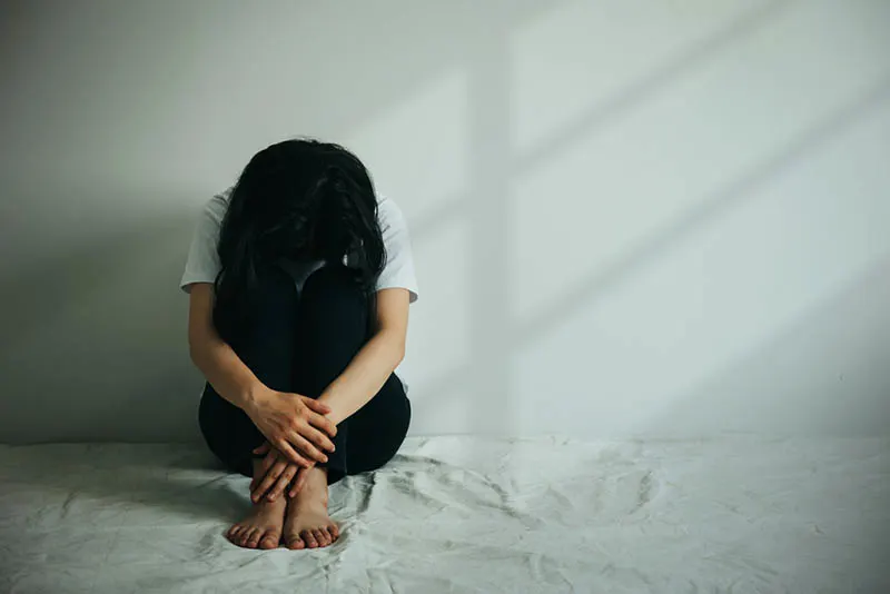 depressive Frau umarmt ihr Knie und weint, während in leeren Raum sitzen