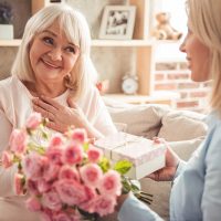 Junge Frau gibt ein Geschenk und Blumen für ihre Schwiegermutter