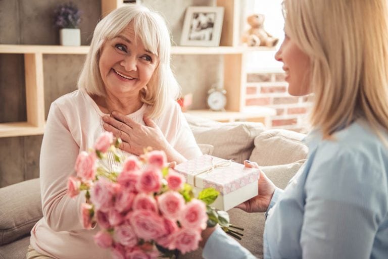 Junge Frau gibt ein Geschenk und Blumen für ihre Schwiegermutter
