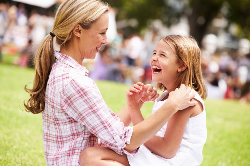 glückliche Mutter lachend mit Tochter im Freien auf dem Gras