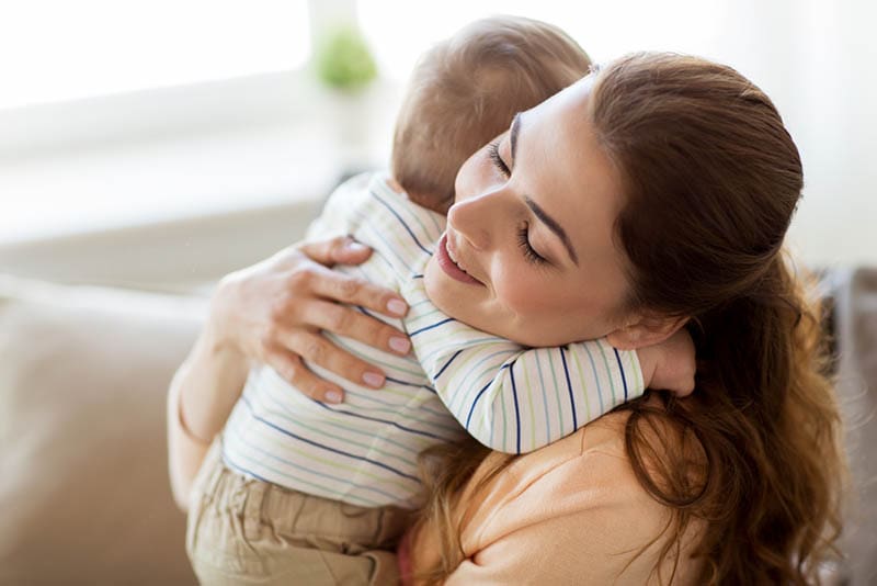 glückliche junge Mutter umarmt fest mit ihrem kleinen Jungen zu Hause