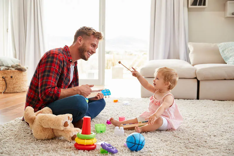 glücklicher junger Vater spielt mit seiner kleinen Tochter auf dem Boden im Wohnzimmer
