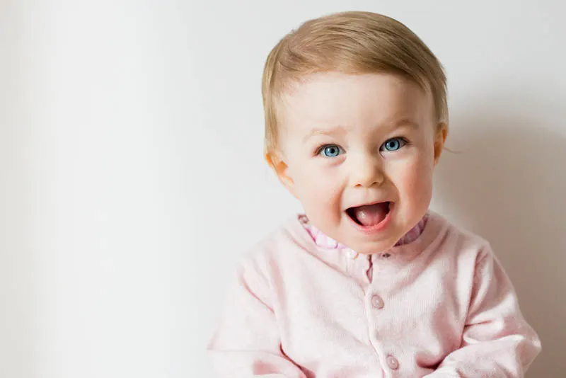 glückliches Baby-Mädchen posiert mit offenem Mund vor einer weißen Wand