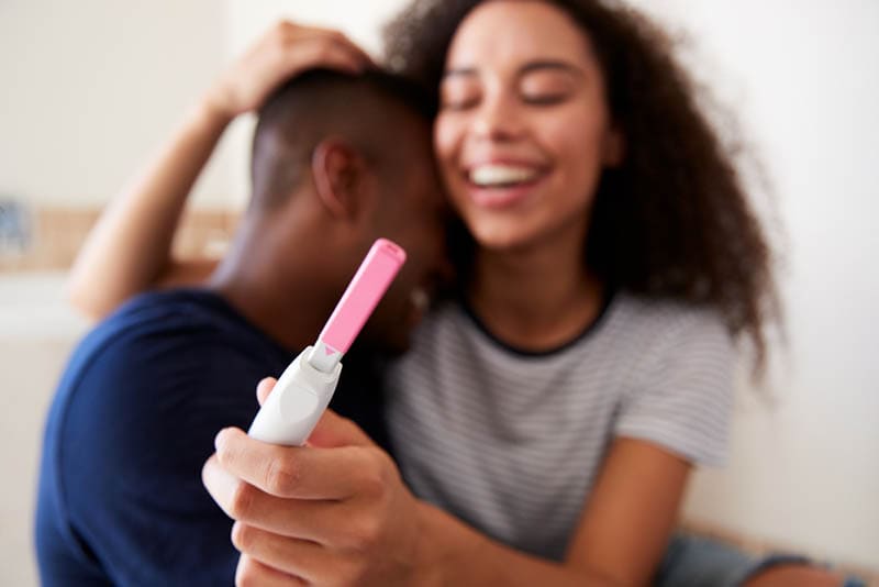 glückliches Paar, das sich umarmt und einen positiven Schwangerschaftstest hält