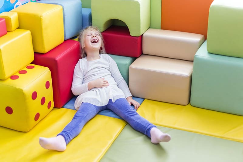 glückliches kleines Mädchen laut lachend auf dem bunten Spielplatz