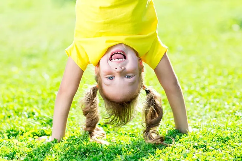 glückliches kleines Mädchen stehend auf Hände im Freien auf dem Gras