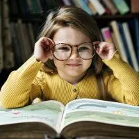 kleines Mädchen trägt große Brille beim Lesen eines Buches
