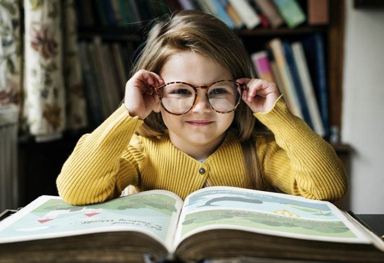 kleines Mädchen trägt große Brille beim Lesen eines Buches