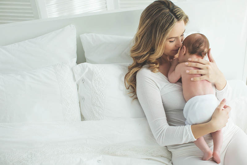 junge Mutter hält neugeborenes Baby auf Brust auf dem Bett