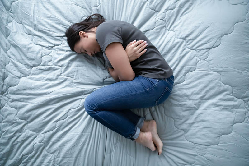 junge depressive Frau auf dem Bett liegend wegen einer Fehlgeburt