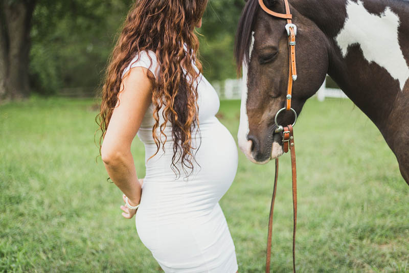 junge schwangere Frau stehend auf dem Gras mit großem Pferd