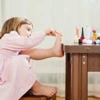kleines Mädchen sitzt auf einem Stuhl, während sie Nagellack auf ihre Zehen setzen