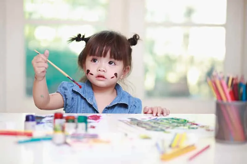 kleines Mädchen hält einen Pinsel und malt am Tisch