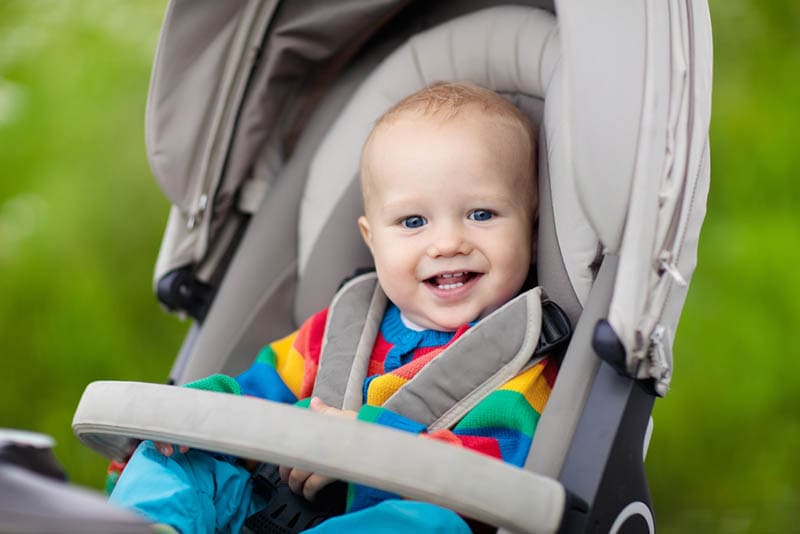 lächelnd Baby Junge sitzt in einem Kinderwagen im Park