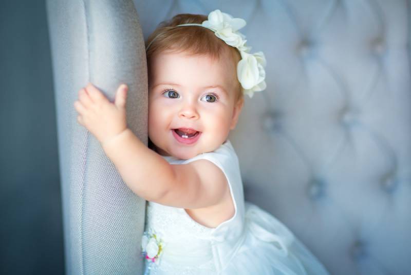lächelnd Baby Mädchen trägt weißes Kleid halten für Stuhl