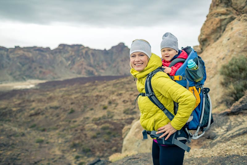 lächelnd Mutter Wandern mit ihrem Baby auf dem Rücken in den Bergen