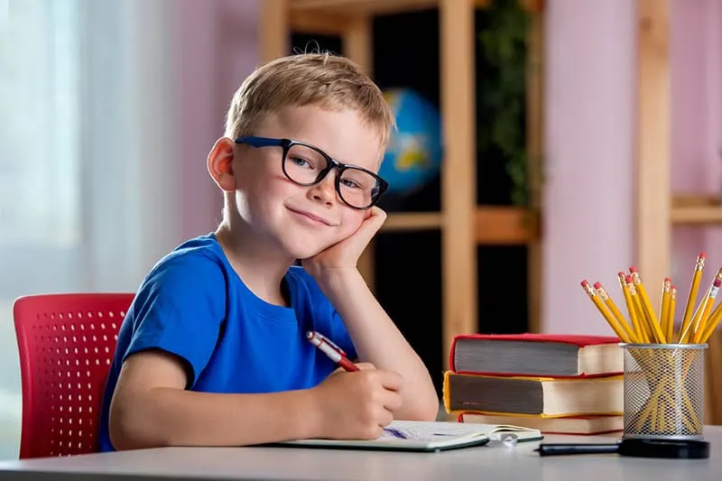 lächelnder kleiner Junge sitzt am Tisch und schreibt in der Schule