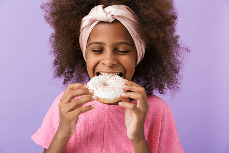 lächelndes Mädchen mit Stirnband isst einen Donut
