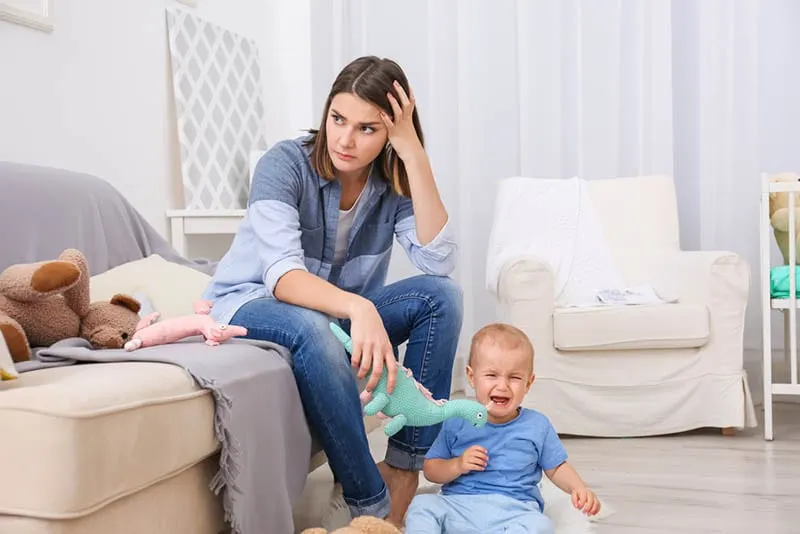 müde gestresste Mutter sitzt auf der Couch, während das Baby weint