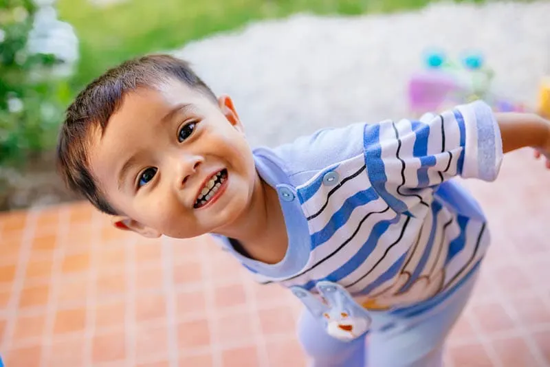 niedliche Baby Junge trägt bunte Kleidung stehen im Freien und lächelnd
