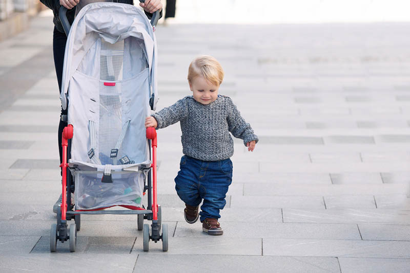 niedliche Baby Junge zu Fuß, während für Kinderwagen im Freien halten