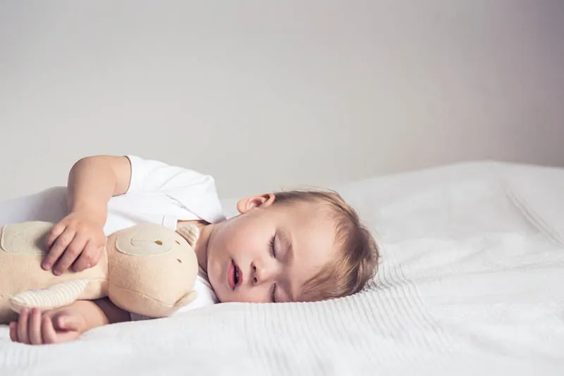 niedlichen Baby Junge schlafen fest auf dem Bett in Umarmung mit Spielzeug