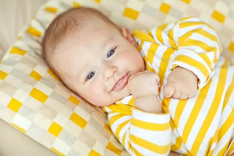niedlichen Baby-Junge trägt gelben Pijama und liegt auf dem Bett
