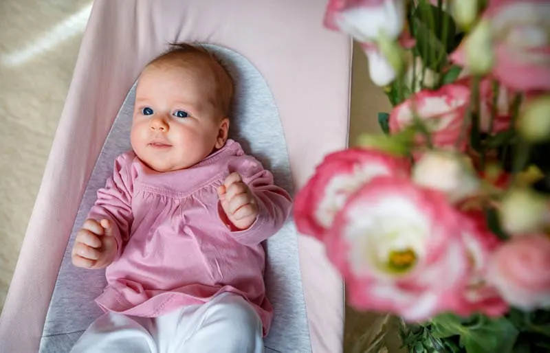 niedlichen Baby-Mädchen liegt in einer Babywippe mit Blumen neben ihr