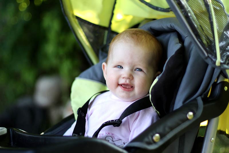 niedlichen Baby-Mädchen sitzt in einem Kinderwagen im Freien und lächelnd