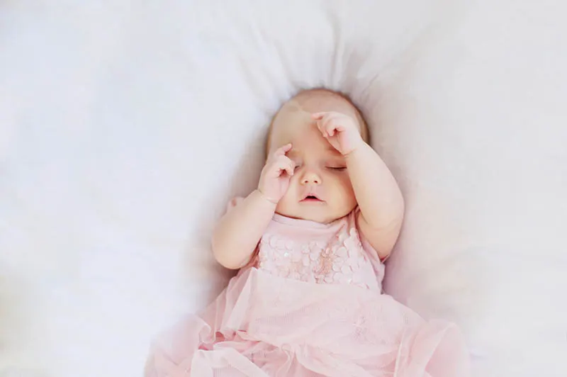 niedlichen Baby Mädchen trägt rosa Kleid schlafen auf dem Bett mit den Händen auf dem Gesicht