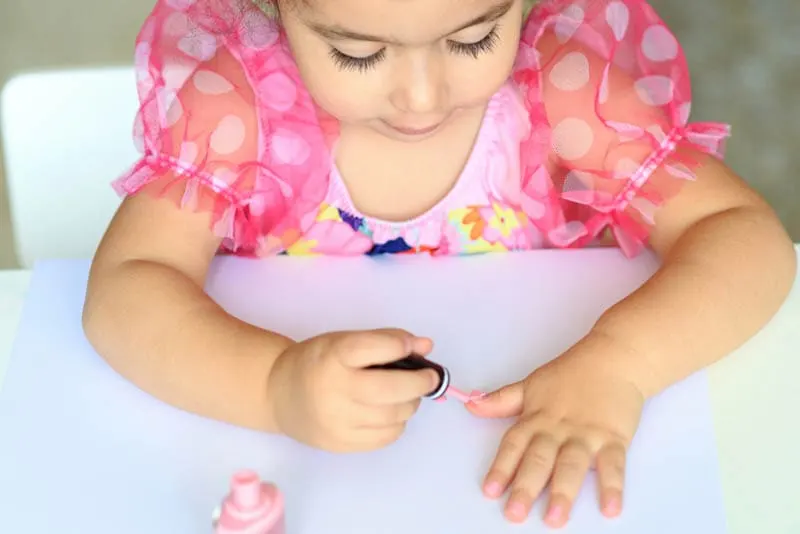 niedlichen Baby Mädchen tun ihren Nagellack auf dem Tisch zu Hause