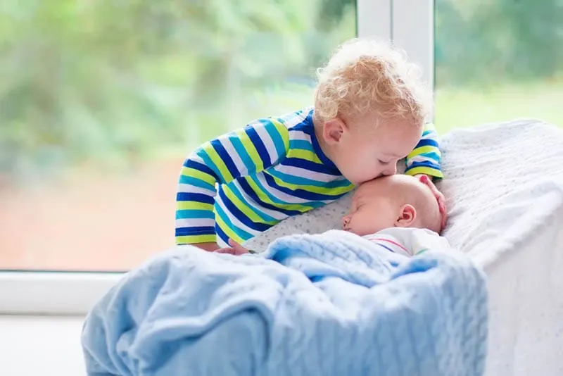 niedlichen kleinen Jungen küssen sein Baby Bruder in einer Babywippe