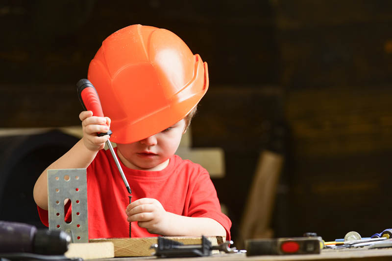 niedlichen kleinen Jungen mit orange Helm auf dem Kopf spielen mit Werkzeug